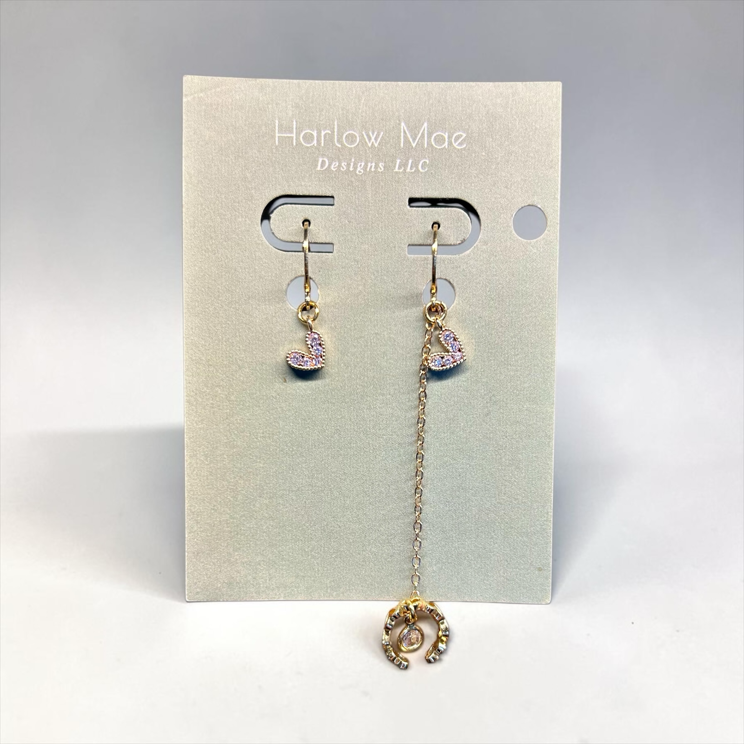 Harlow Mae Designs LLC asymmetrical gold-tone drop earrings with heart charms and cubic zirconia stones.