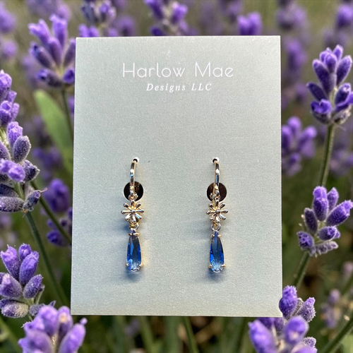 Harlow Mae delicate gold-tone star flower drop earrings with faceted blue gemstone accents.
